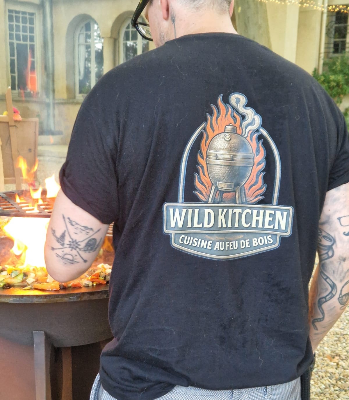 Chef Wild Kitchen en action devant le brasero avec t-shirt logo